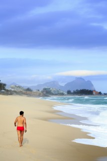 Hispanic man walking on beach near waves