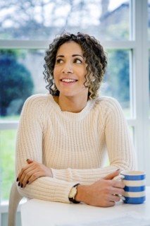 Curious woman sitting at table holding coffee cup