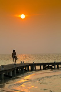 Mixed Race woman standing on ocean dock at sunset