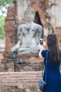 Asian woman photographing Buddha statue with cell phone