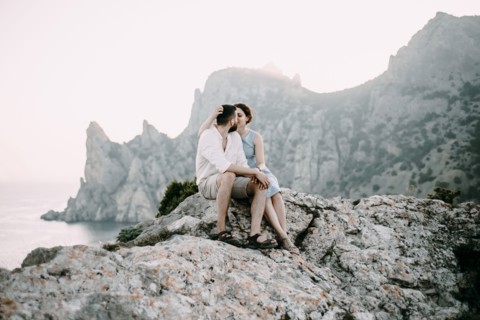 Caucasian couple sitting on rocks at lake