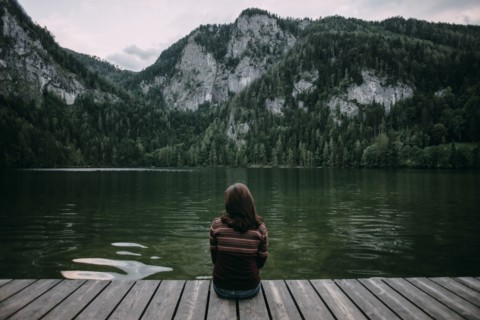 Caucasian woman sitting on dock admiring scenic view of mountain