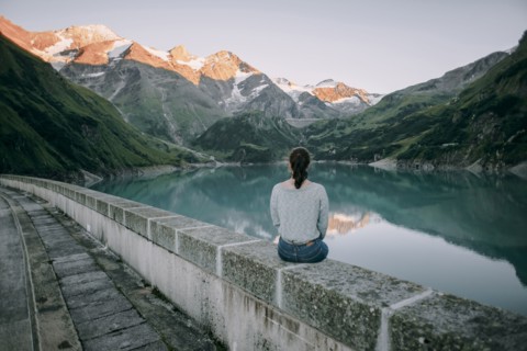 Caucasian woman sitting on wall at mountain lake