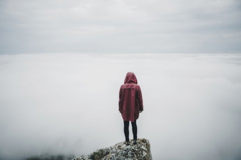 Distant Caucasian woman standing on rock watching fog on ocean