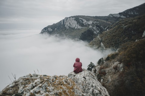 Distant Caucasian woman sitting on rock watching fog on ocean