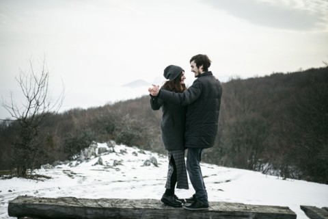 Caucasian couple dancing on log in winter