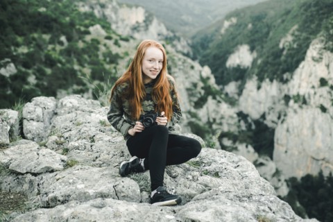 Portrait of smiling Caucasian woman sitting on rock holding camera