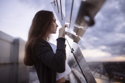 Curious Caucasian woman peering over glass wall at scenic view