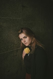 Serious Caucasian woman leaning on wall holding flower