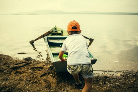 Caucasian boy pushing boat into still lake