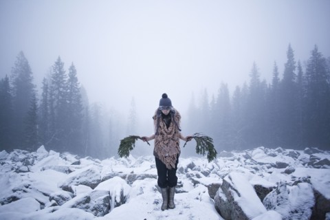Caucasian woman holding tree branches on snow covered rocks