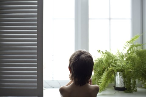 Asian boy looking out bedroom window