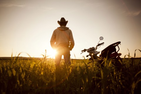 Mari man standing in field with motorcycle