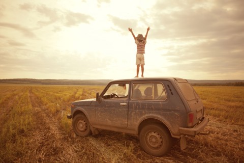 Mari boy standing on car roof in rural field