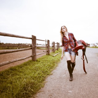 Caucasian woman carrying horse saddle on ranch