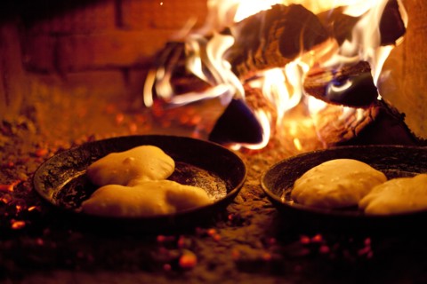 Close up of pastries cooking in skillets near wood fire