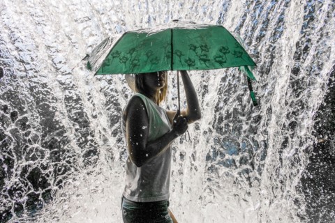 Caucasian woman holding umbrella near splashing water
