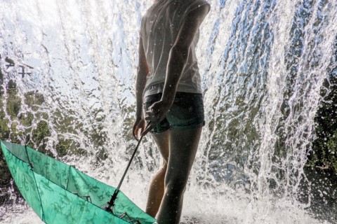 Caucasian woman holding umbrella near splashing water