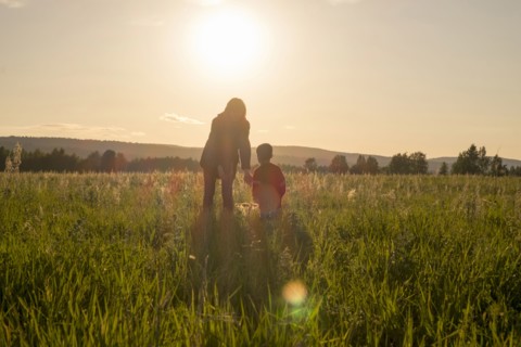 Woman and son standing in field at sunset