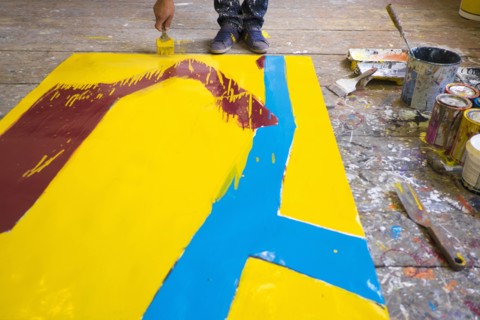 Legs of Mari man painting canvas on floor