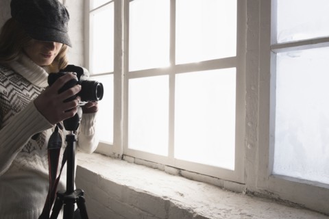 Caucasian woman near window photographing with camera