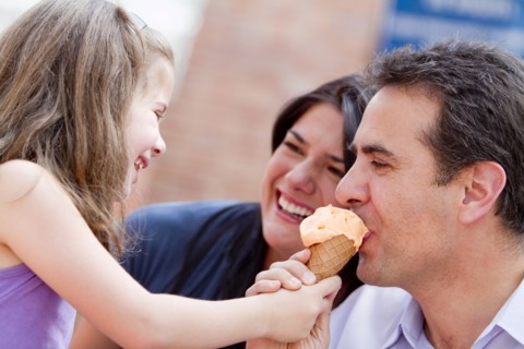 Hispanic girl giving father a bite of her ice cream cone