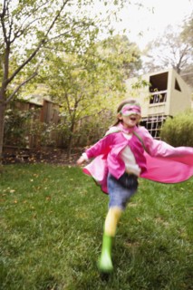 Middle Eastern girl wearing cape and mask running in backyard