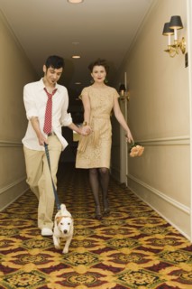 Young coupled dressed up walking down hotel hallway with dog