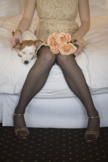 Woman in fancy dress with dog and flowers sitting on bed