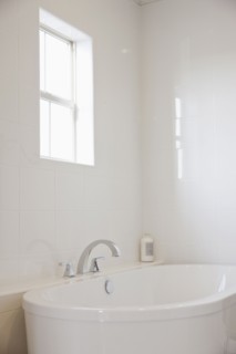 Close-up of a white bath with tiled wall and window in the bathroom