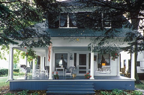Pretty Summer cottage home with large front porch with columns. Porch all around. Dormer windows. American Flag