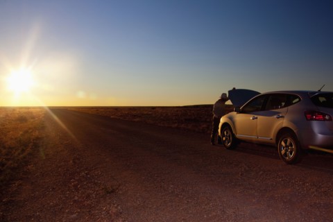 Person opening hood of car on remote road