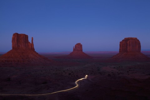 Long exposure of car driving past butte rock formations in desert landscape