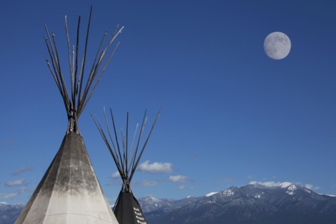 Teepees under full moon in blue sky
