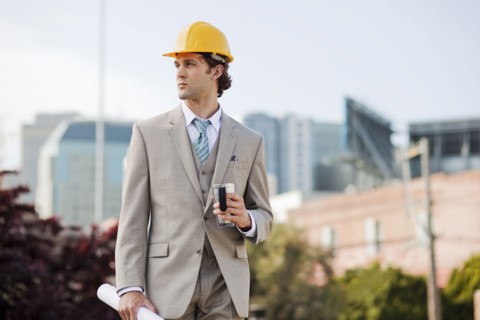 Hispanic businessman drinking coffee and carrying blueprint outdoors