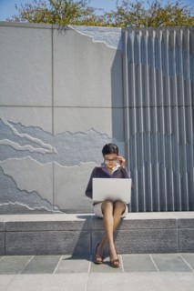 Asian businesswoman sitting on concrete wall using laptop