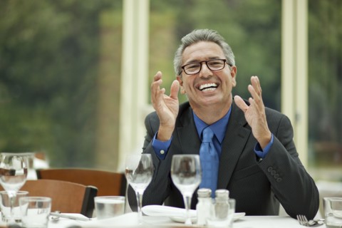 Excited Hispanic businessman sitting at table in restaurant