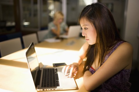 Asian businesswoman using laptop in communal workspace