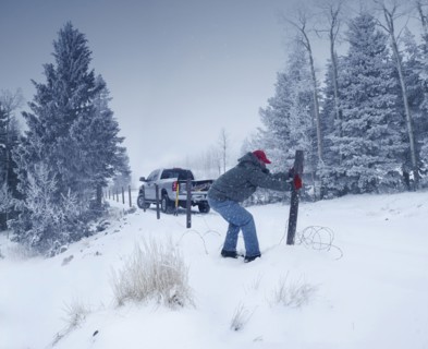 Man repairing wooden post in snowy ground
