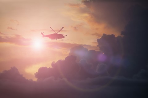 Silhouette of helicopter flying in cloudy sky