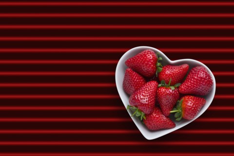 Strawberries in heart-shape bowl on red striped background
