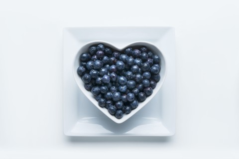 Blueberries in heart-shape bowl on white background