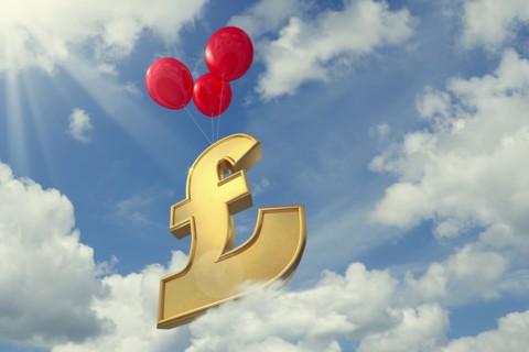 Red balloons lifting British pound symbol in cloudy sky