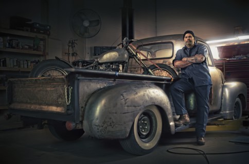 Caucasian mechanic posing on vintage truck with motorcycle