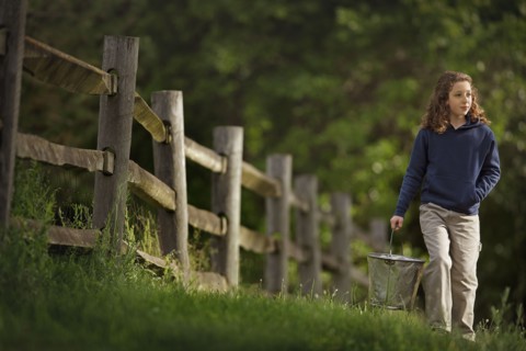 Caucasian girl carrying bucket near wooden fence