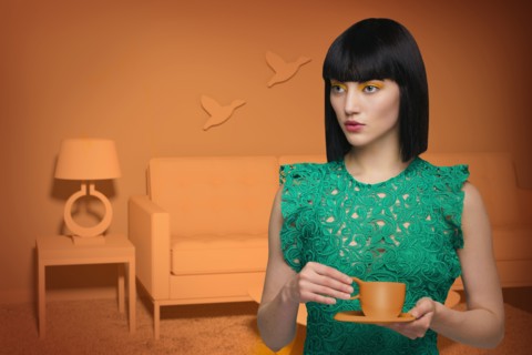 Caucasian woman in orange old-fashioned livingroom drinking coffee