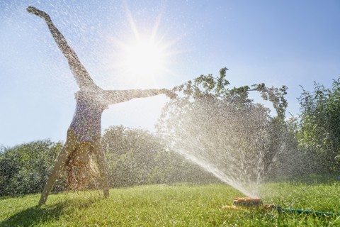 Caucasian girl performing cartwheel through backyard sprinkler