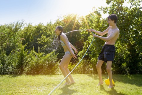 Caucasian boy spraying sister with hose in backyard