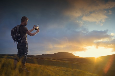 Caucasian hiker photographing sunset with digital tablet