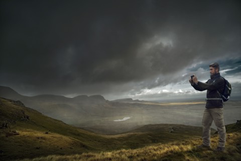 Caucasian hiker photographing storm clouds over landscape